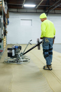 An ECS employee using the stainless steel bladed power trowel on the grout layer in heavy duty epoxy floor coating in kansas city