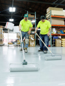2 ECS employees laying down the final epoxy coat on heavy duty epoxy floor coating in a warehouse